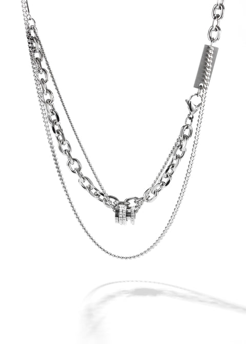 A double chain necklace, featuring a chunky cross chain. At the center, there's a small, distinct cross pendant, and it secures with a barrel clasp embellished with crystals.