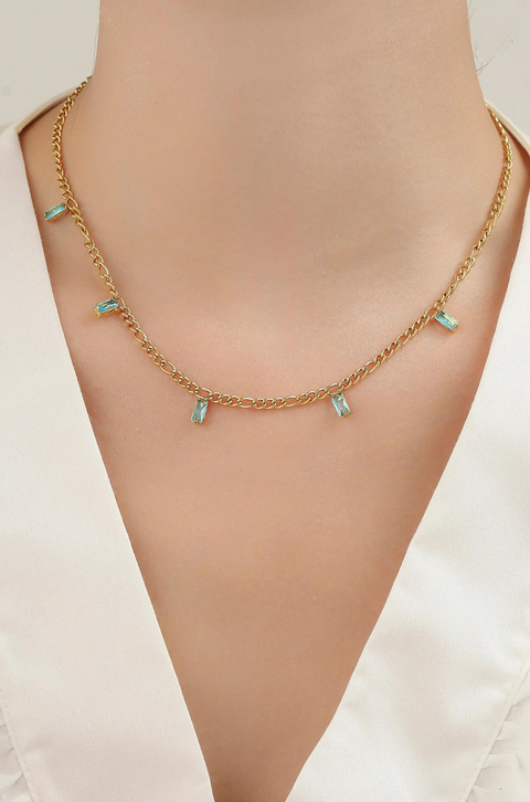A gold baguette necklace featuring small rectangular aqua-colored crystals along the chain.