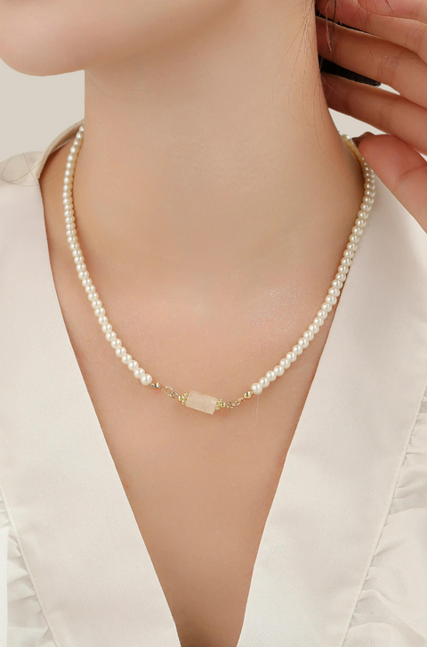 This pearl with pendant necklace features a string of shiny pearls with a soft stone in the center.