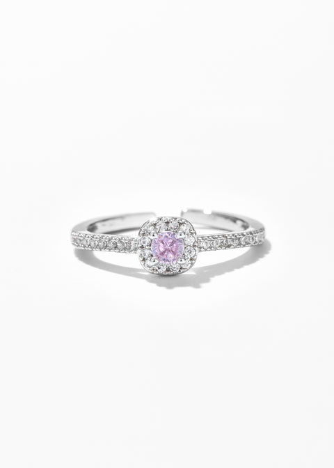 A square ring with a central pink gemstone surrounded by tiny clear stones set in a gold plated ring.