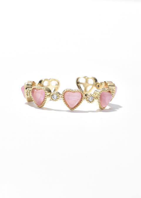 A pink stone ring with a band of small, heart-shaped pink stones, each framed in gold and separated by tiny clear gems.