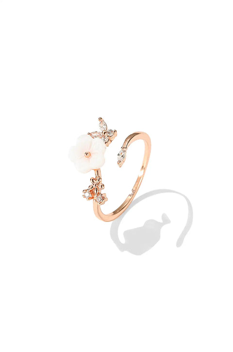 A rose gold flower ring featuring white flower, and tiny diamond-like stones.