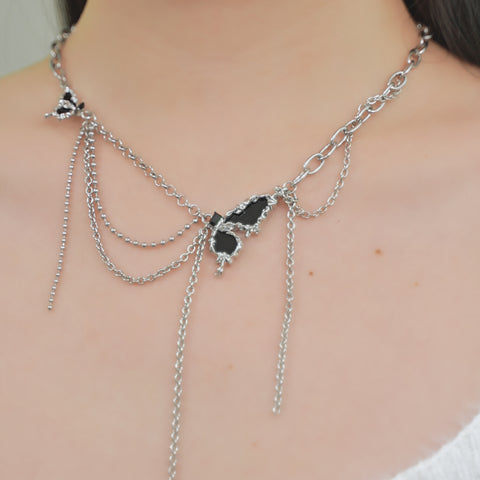 A butterfly necklace with a silver chain, adorned with two butterfly pendants and layered chains that drape with black gemstone accents.