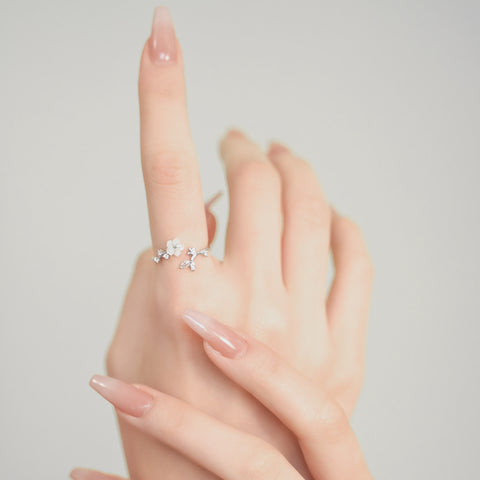 A silver open ring featuring a floral ring design, complemented by small crystal details along the petals and band.