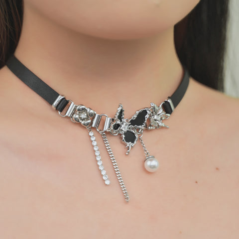 A butterfly collar with a black band, complemented by a mix of shiny elements, a hanging pearl charm, and chain tassels.