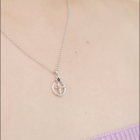 One of the matching couples necklaces with a silver cross pendant featuring a black diamond-shaped stone at the intersection of its cross design.