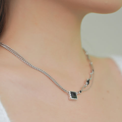 A square pendant necklace with additional small black stones along one side of the chain.