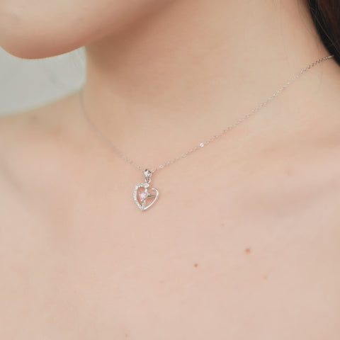 One of the matching couples necklaces with a silver cross pendant that has a smaller pink stone in the center and part of the heart outlined with tiny crystals.