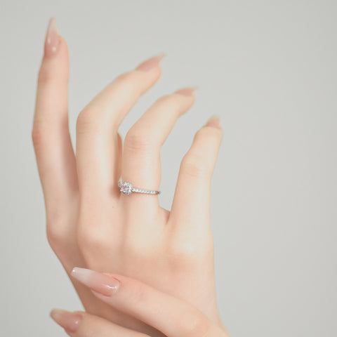 A square ring with a central pink gemstone surrounded by tiny clear stones set in a gold plated ring.