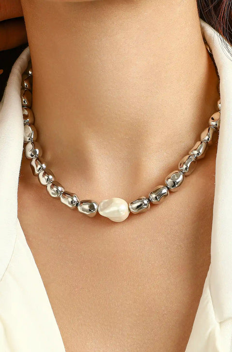 A silver beaded necklace featuring shiny, smooth beads with a single, larger asymmetrical pearl.