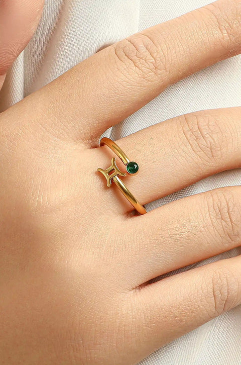 Gemini ring jewelry in gold featuring the zodiac symbol adorned with a small green gemstone.