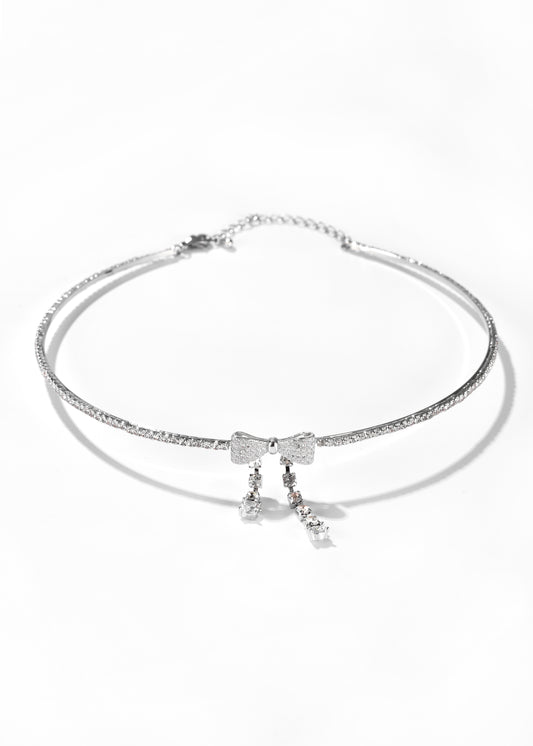A white gold choker necklace with a bow design and hanging clear crystal details.