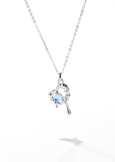 An opal necklace with a delicate chain and a silver heart pendant that has a lava design cradling a small opal at the center, flanked by tiny sparkling stones.