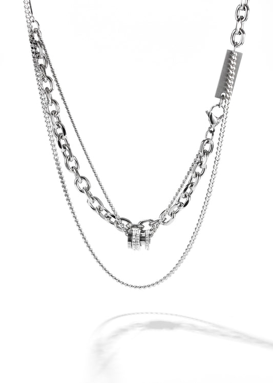A double chain necklace, featuring a chunky cross chain. At the center, there's a small, distinct cross pendant, and it secures with a barrel clasp embellished with crystals.