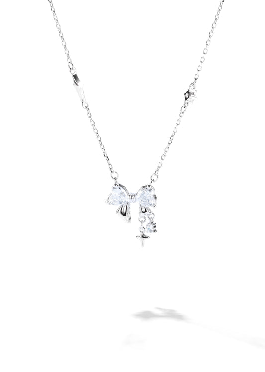 A bow necklace with a thin silver chain, featuring a central bow-shaped pendant with crystal detailing and small star-shaped charms along the chain.