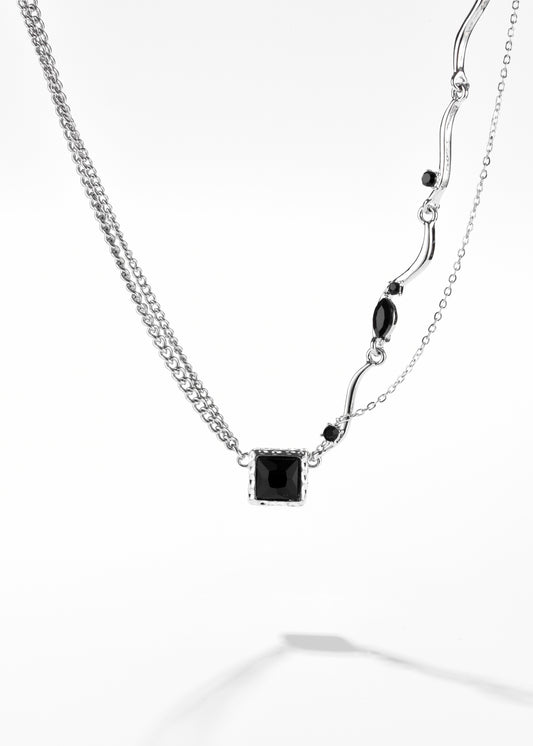 A square pendant necklace with additional small black stones along one side of the chain.