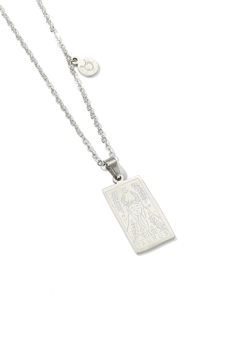 A Taurus necklace featuring rectangular pendant with floral design, and a smaller, round charm with the zodiac sign.