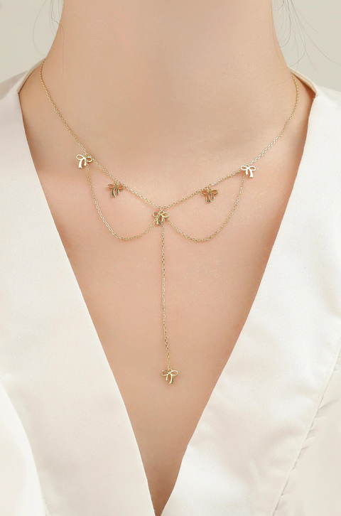 A silver bow necklace featuring small bow charms evenly spaced on a chain.