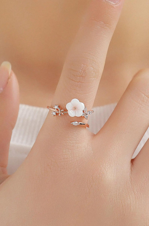 A rose gold flower ring featuring white flower, and tiny diamond-like stones.