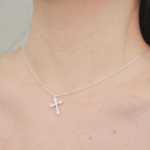 A silver cross necklace with a simple chain and a distinctive cross pendant.