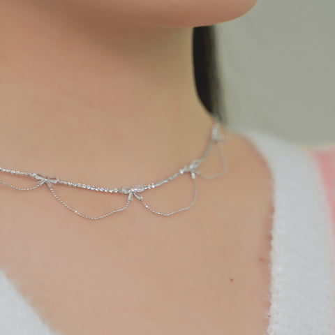 A silver bow knot necklace choker with a chain design, featuring small, shining crystals at intervals.