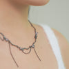 Bow necklace with gunmetal chain links, small bow motifs and pale pink gemstones.