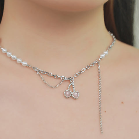 Cherry necklace in silver chain and a strand of white pearls, leading to a pink heart pendant.