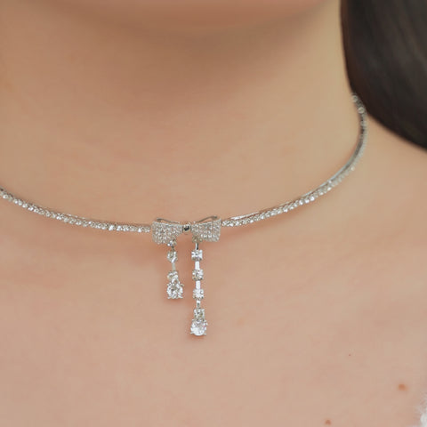 A bow choker necklace with hanging clear crystal details.