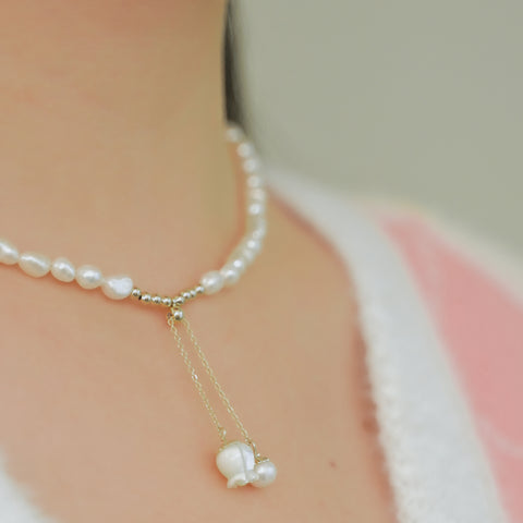 Freshwater pearl necklace forming a chain and a small gold flower pendant hanging from a gold chain lariat.