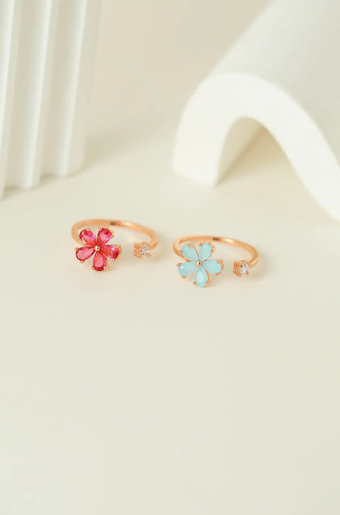 Dainty gold rings featuring gemstone flower, with a small clear stone on the opposite end.